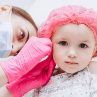 Charming little girl having an ear piercing process